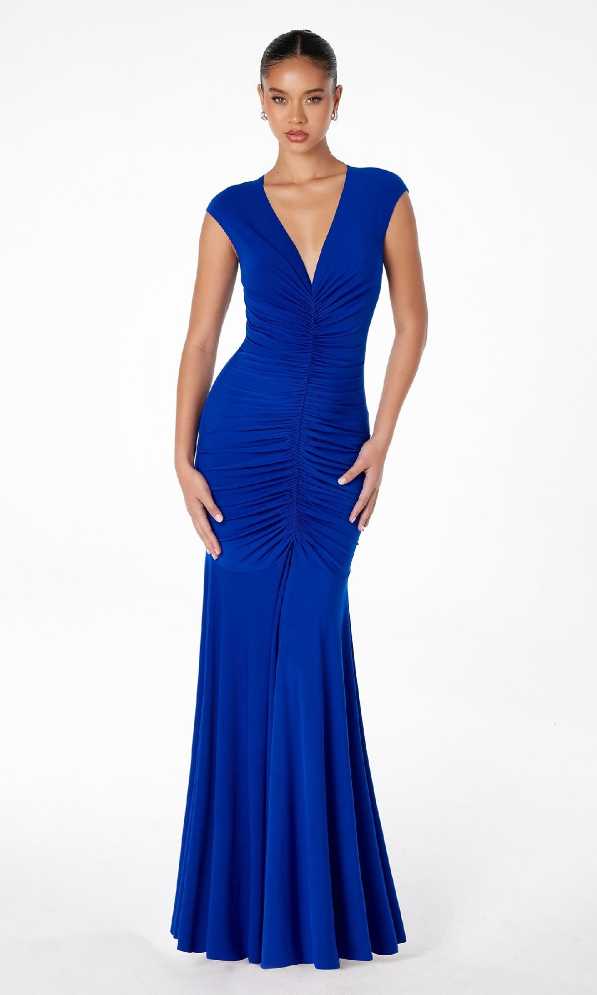 A woman models the Cap-Sleeve Long Ruched Prom Dress: Astee T2009, a fitted royal blue gown with cap sleeves and a deep V-neckline, posing against a plain white background.